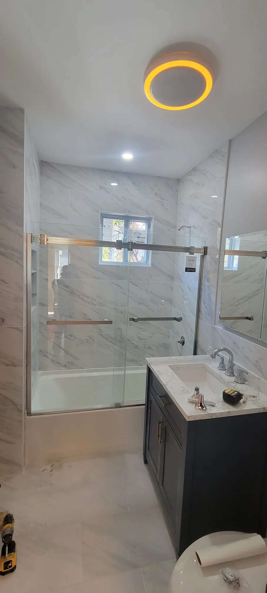 Bathroom renovation in progress with marble tile, glass doors and navy vanity