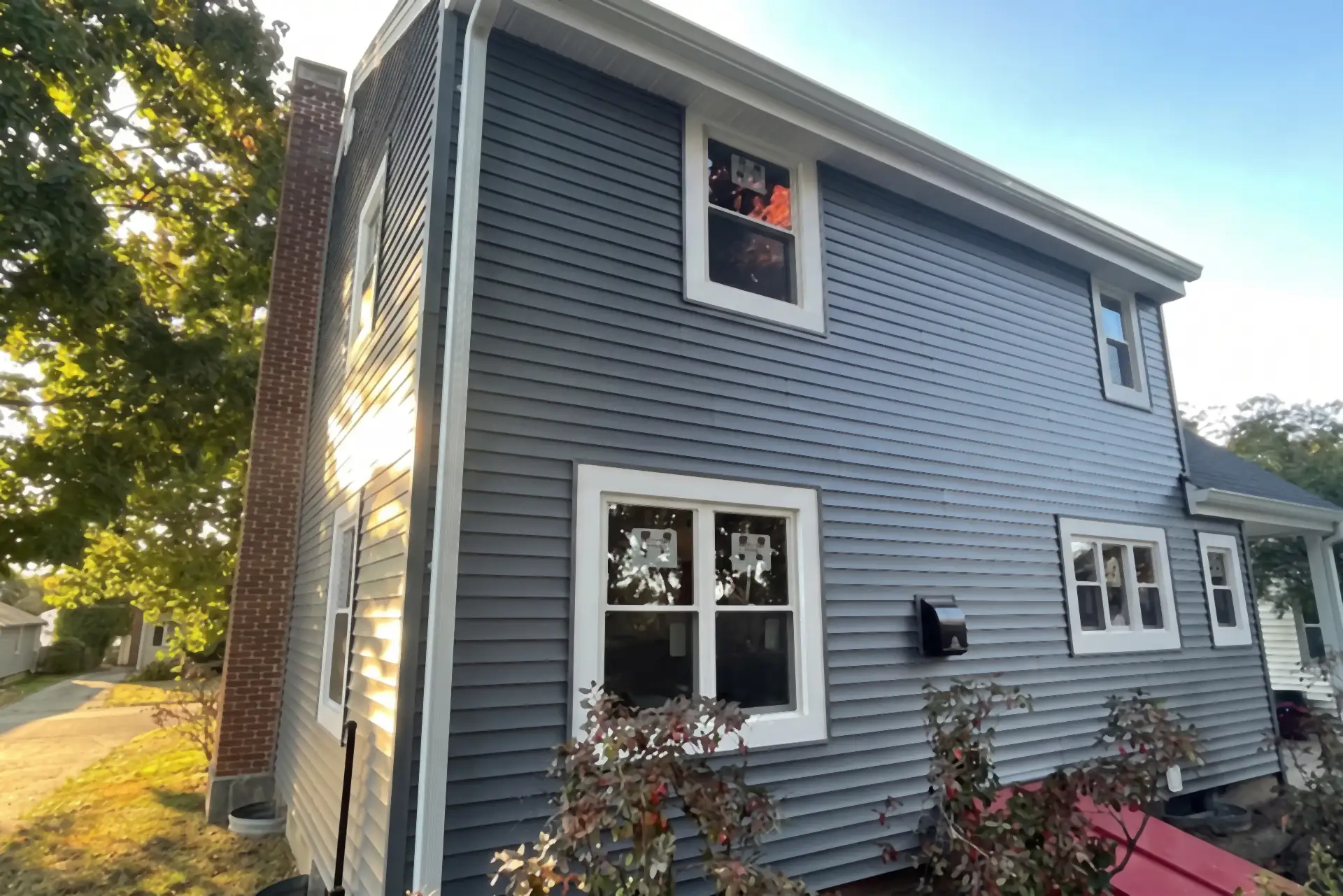 Completed blue vinyl siding house exterior with white trim and brick chimney