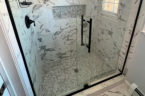 Marble-tiled walk-in shower with glass door, mosaic floor and black fixtures