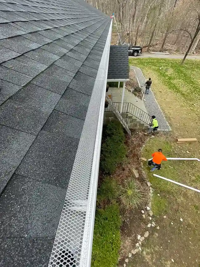 New metal gutter guard along roof edge with workers installing drainage below