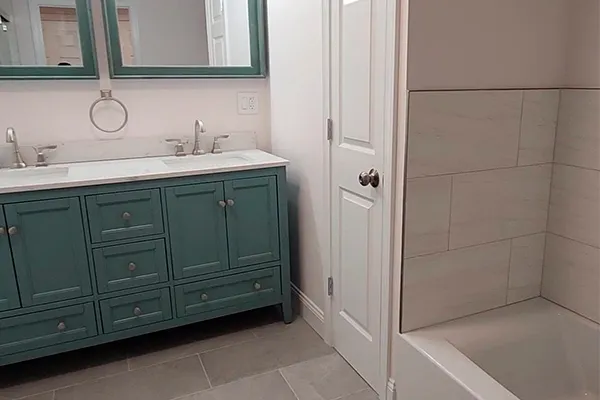 Renovated bathroom with green double vanity, marble counters and tiled shower in Connecticut
