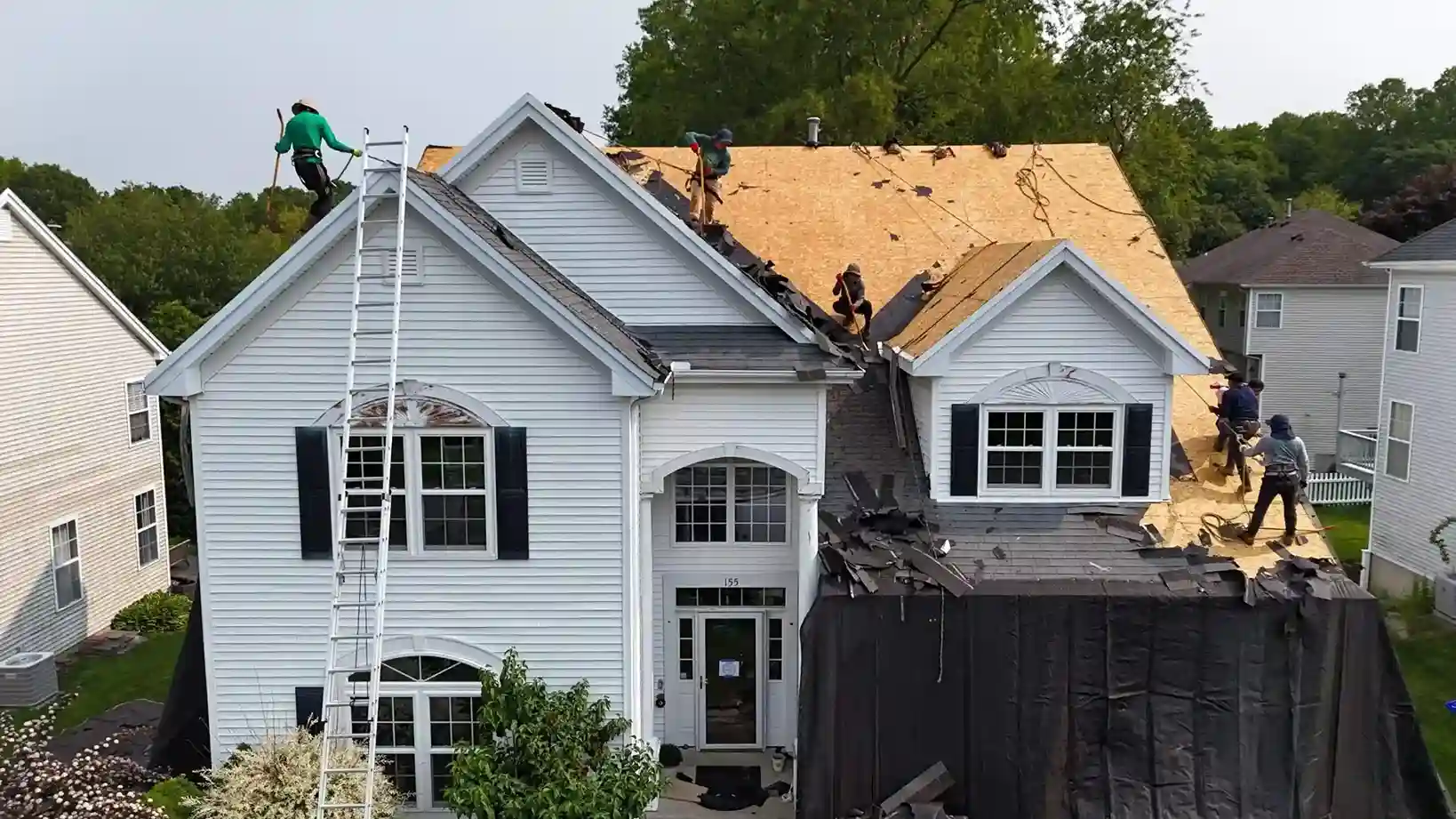 Aerial view of roofers tearing off old shingles on white Connecticut house roof replacement