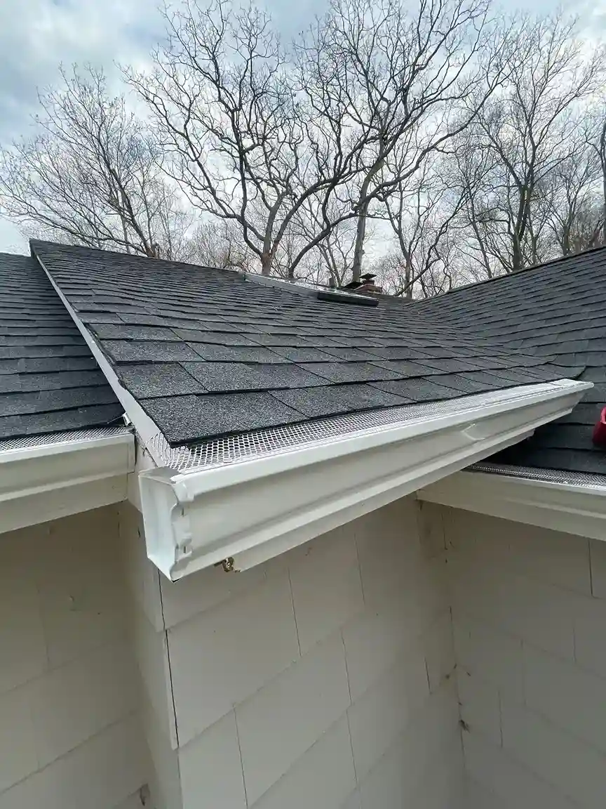 White seamless gutter with mesh guard and downspout on asphalt shingle roof