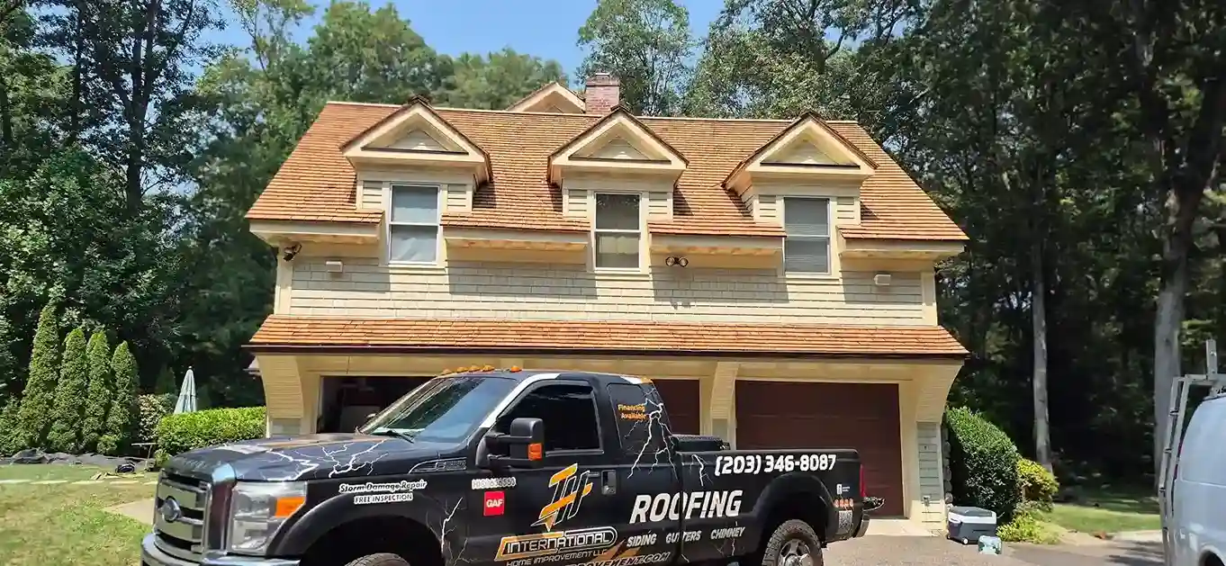 Yellow two-story house with new wood shake roof and three dormers, branded roofing truck